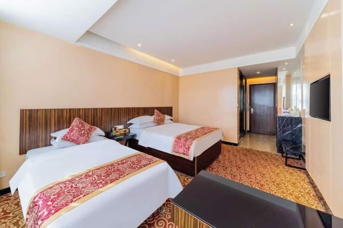 A hotel room with two beds, a TV, and a desk.
