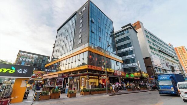 A multi-story building with a glass facade, a ground-level commercial area with shops, and a parking area with vehicles. - Shenzhen Jiehao Business Hotel (Bao'an Airport Guyi Subway Station) (Shenzhen)