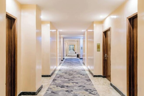 A hotel hallway with a carpeted floor, doors on both sides, and a light-colored wall.
