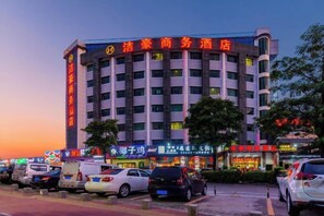 A multi-story hotel with a prominent sign, a parking lot with several cars, and a clear sky.