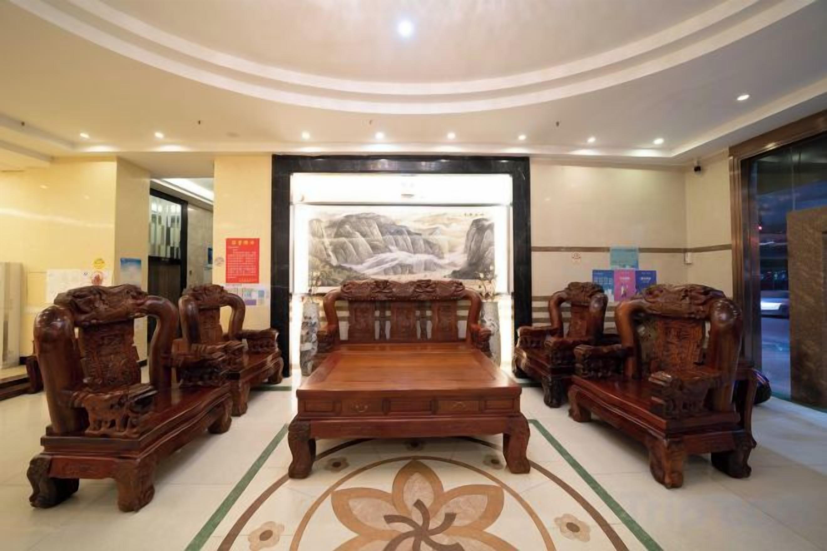A lobby with a central wooden sofa set, a large painting on the wall, and a patterned floor design.
