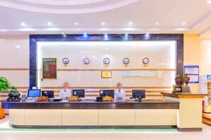 A hotel reception area with a reception desk, multiple monitors, a clock, and framed certificates on the wall.