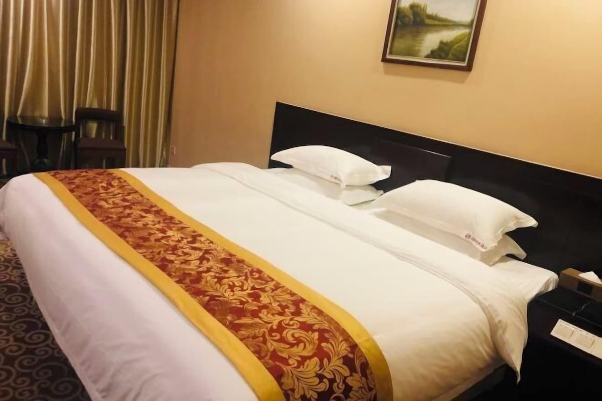 A hotel room with a bed, a nightstand, a chair, and a painting on the wall.