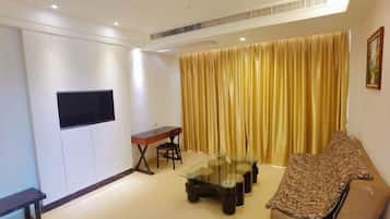 A living room with a sofa, a glass coffee table, a TV mounted on the wall, and a curtain.