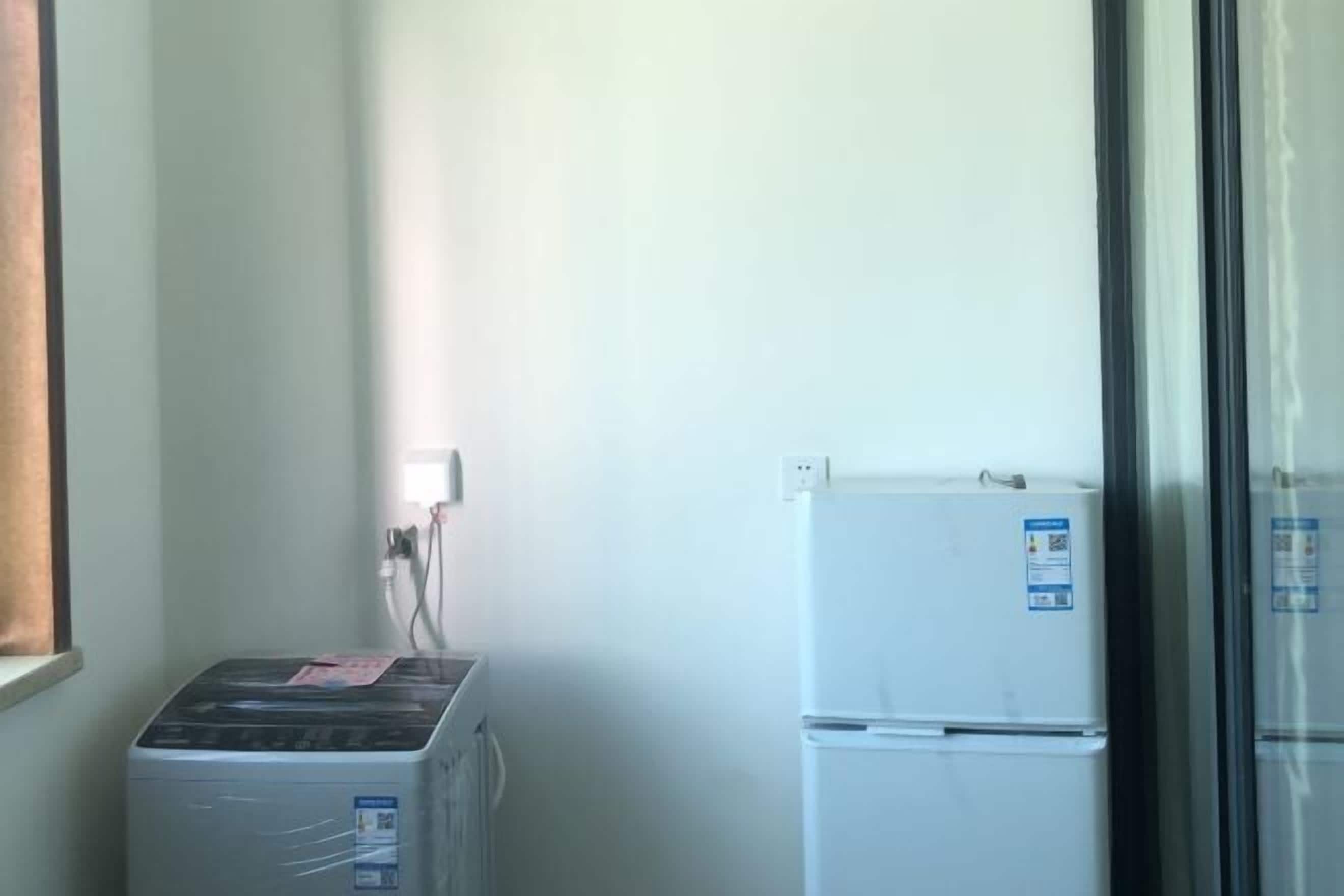 Ein kleines Zimmer mit Waschmaschine, Kühlschrank und einem Fenster mit Jalousien.