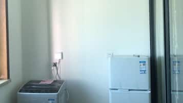 Ein kleines Zimmer mit Waschmaschine, Kühlschrank und einem Fenster mit Jalousien.
