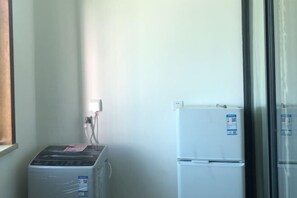 A small room with a washing machine, a refrigerator, and a window with blinds.
