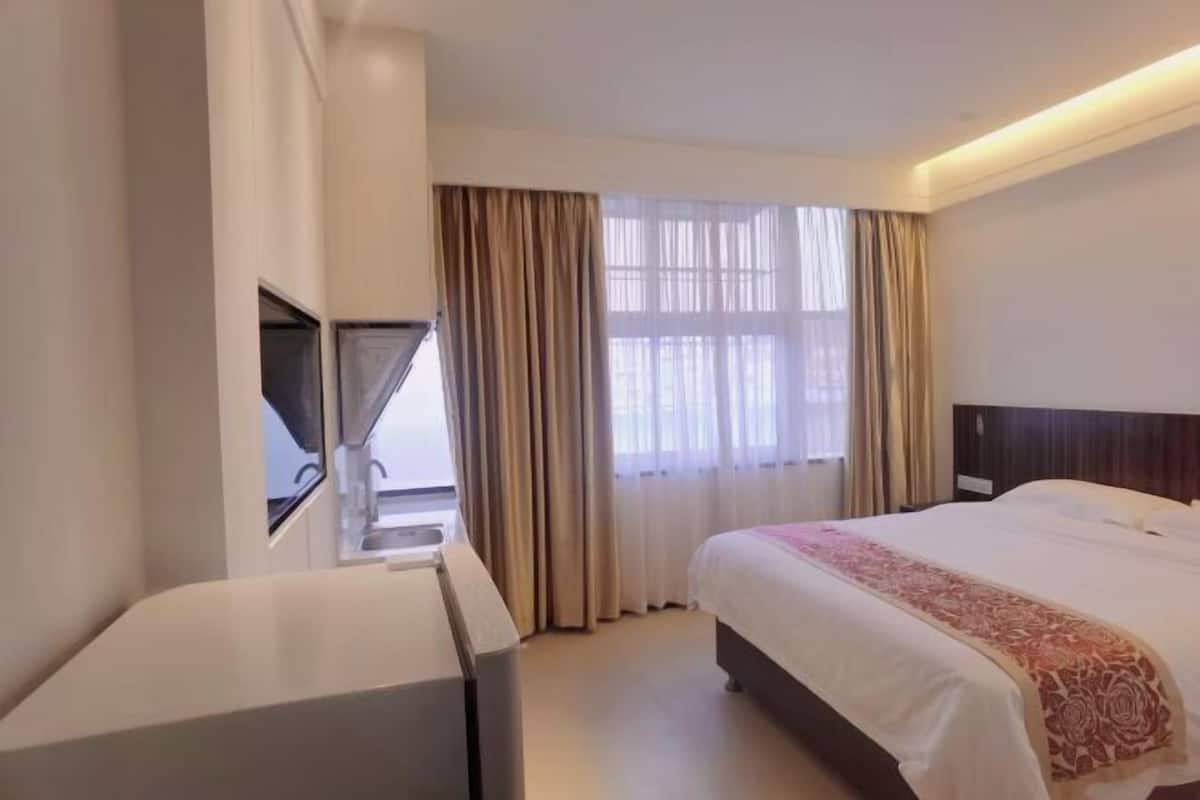 A hotel room with a bed, a desk, a window with curtains, and a view of the outside.