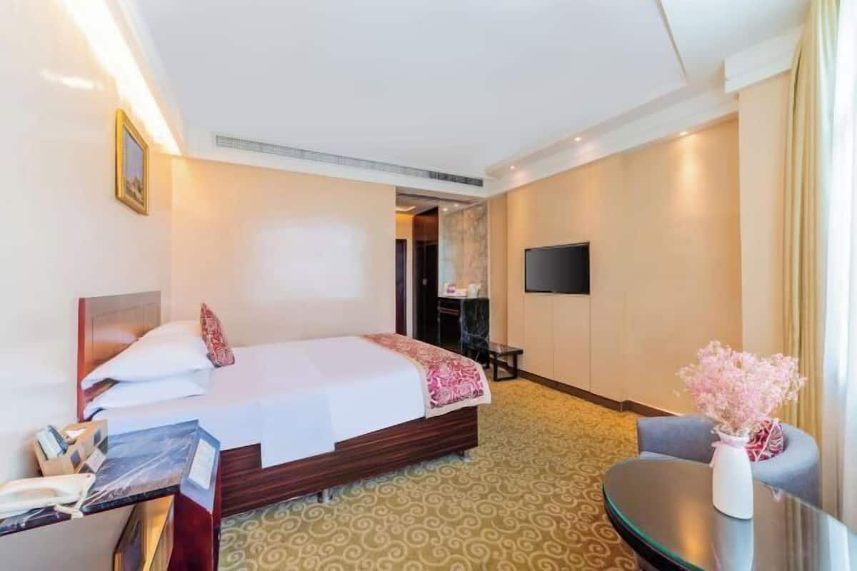 A hotel room with a bed, a desk, a chair, a TV, and a vase with flowers.