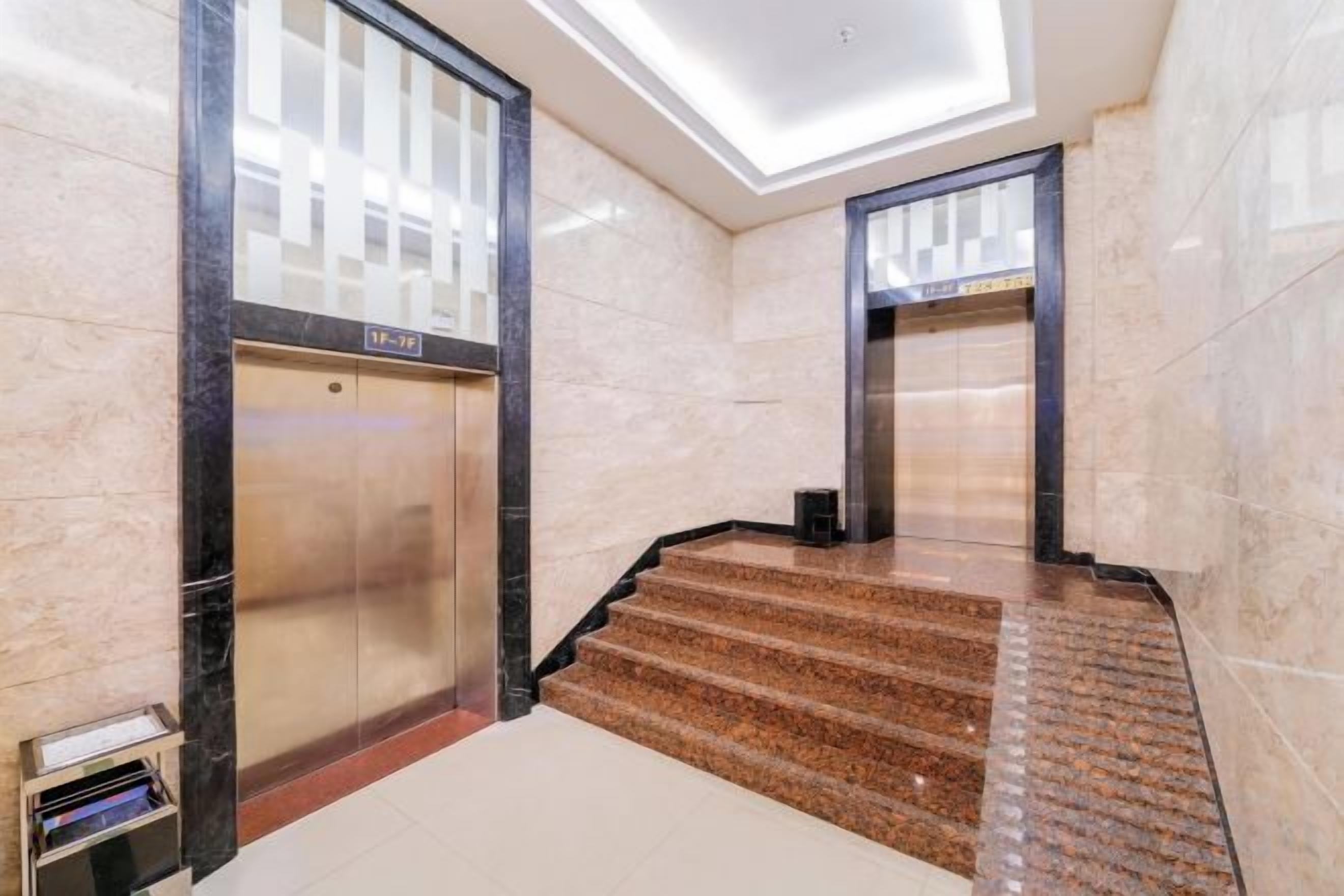 A hotel lobby with marble flooring, a staircase, and two elevators.