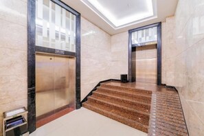 Un hall d’hôtel avec un sol en marbre, un escalier et deux ascenseurs.