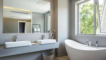 Un baño moderno con un espejo grande, dos lavamanos y una bañera independiente.