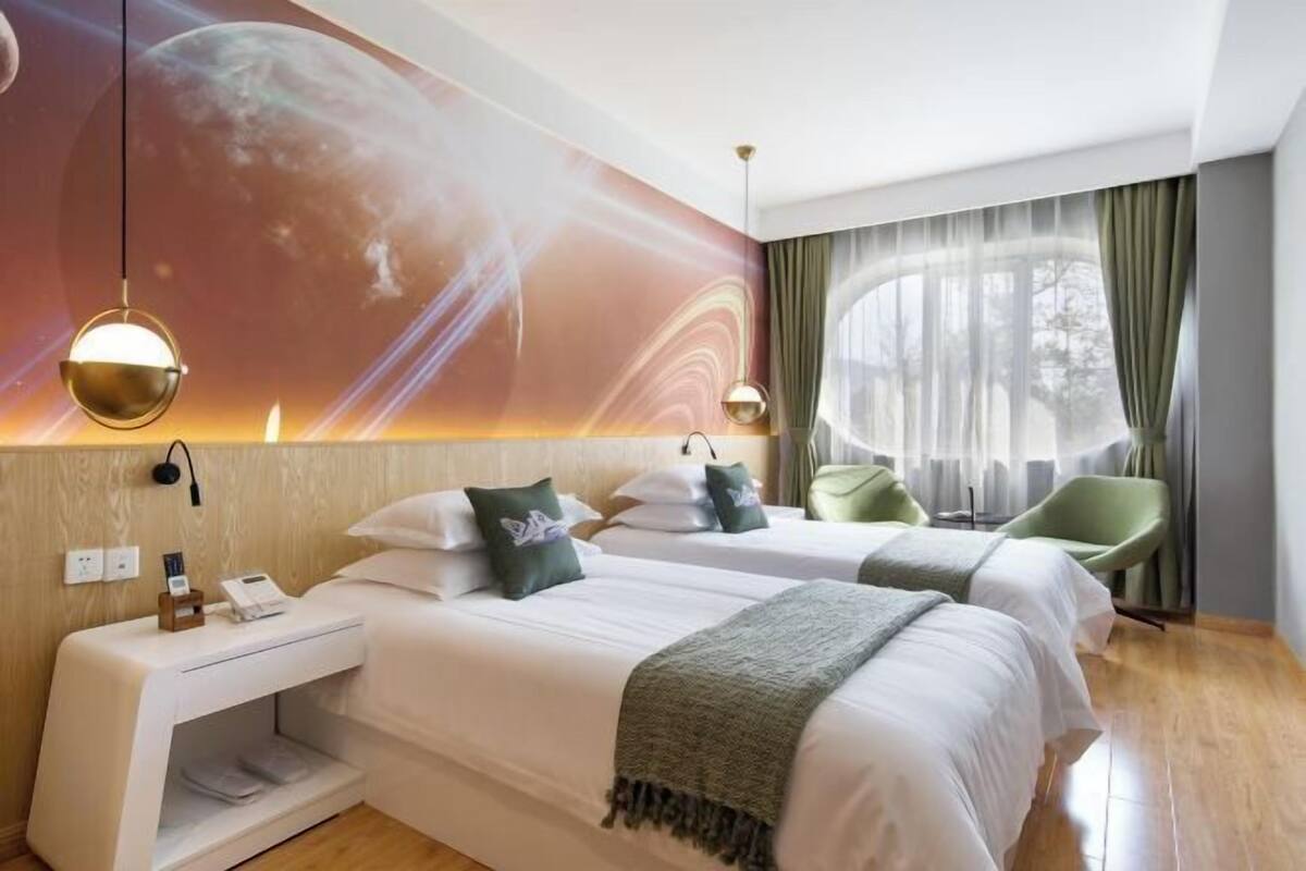 A hotel room with two beds, a nightstand with a phone, and a wall mural.