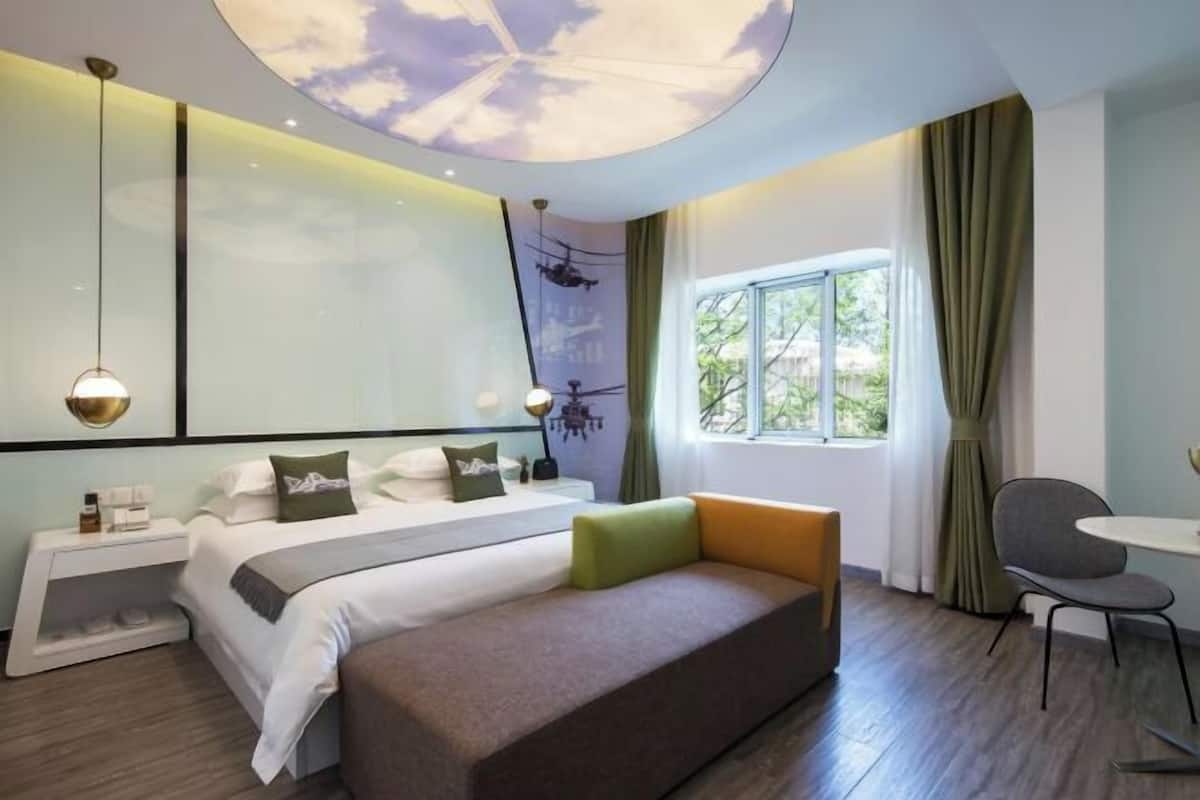 A modern hotel room with a bed, a sofa, a desk, and a window with curtains.