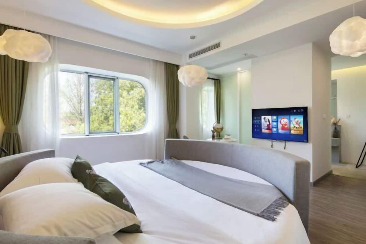 A modern hotel room with a large bed, a television, and a window with curtains.
