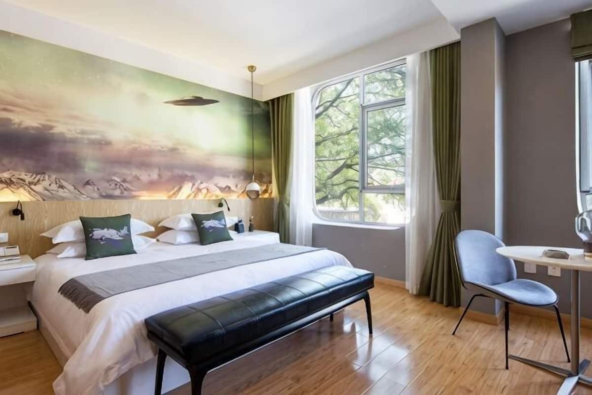 A bedroom with a bed, a bench, a desk, and a window with curtains.