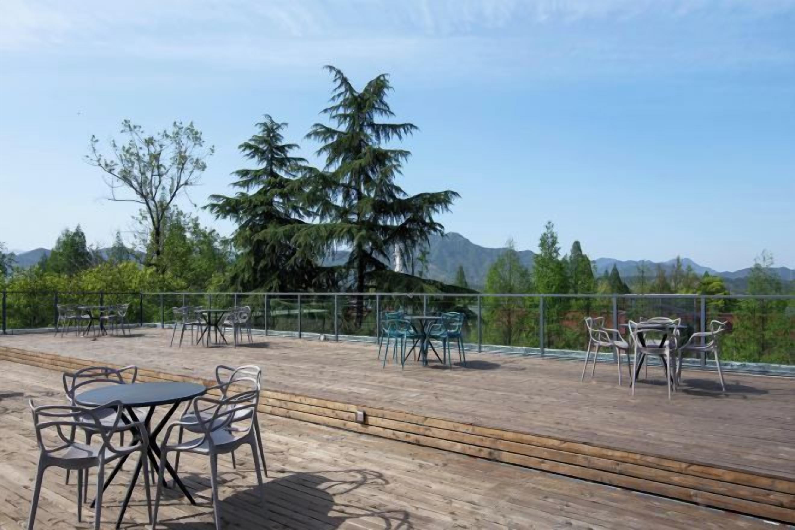 Une terrasse extérieure avec des tables et des chaises, entourée d’une plateforme en bois et d’une clôture en métal, offrant une vue sur un paysage montagneux.