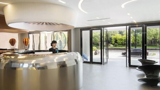 A modern hotel lobby with a reception desk, large glass doors leading to the outdoors, and a seating area with black chairs. - Happy Air Hotel (Jiande) (Jiande)