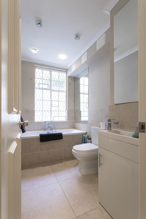 A bathroom with a bathtub, toilet, and a window with a grid pattern.