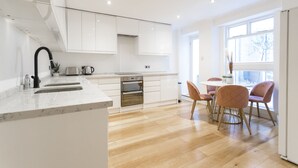 Una cucina moderna con mobili bianchi, un piano di lavoro in marmo e un forno integrato. C'è un'area pranzo con un tavolo rotondo e sedie rosa.