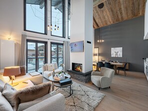 A modern living room with a fireplace, large windows, and a dining area. - New apartment in Courchevel, sauna, fireplace, parking (Courchevel 1550)