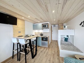 A compact, modern room with a kitchenette, a dining area, and a bunk bed.