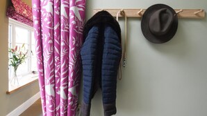 A room with a window, pink curtains, a coat rack with a hat, and a vase with flowers. - Boutique Farm stay cottage in Worcestershire - Hot Tub / Dog Friendly (worcester)