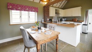 A kitchen with a wooden dining table, chairs, a window with blinds, a brick fireplace, and a kitchen island with a sink and microwave. - Boutique Farm stay cottage in Worcestershire - Hot Tub / Dog Friendly (worcester)
