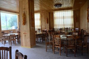 A wooden interior with multiple tables and chairs, large windows, and a high ceiling.