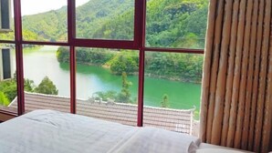 A room with a large window overlooking a river and forested hills. - Nongfu Hostel (Rongshui)