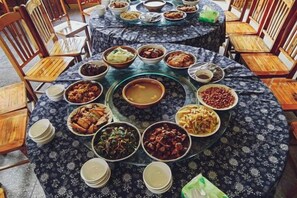A round dining table with multiple dishes and bowls, surrounded by wooden chairs. - Nongfu Hostel (Rongshui)