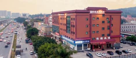 A multi-story hotel with a red facade, a parking lot, and a busy street in the background.