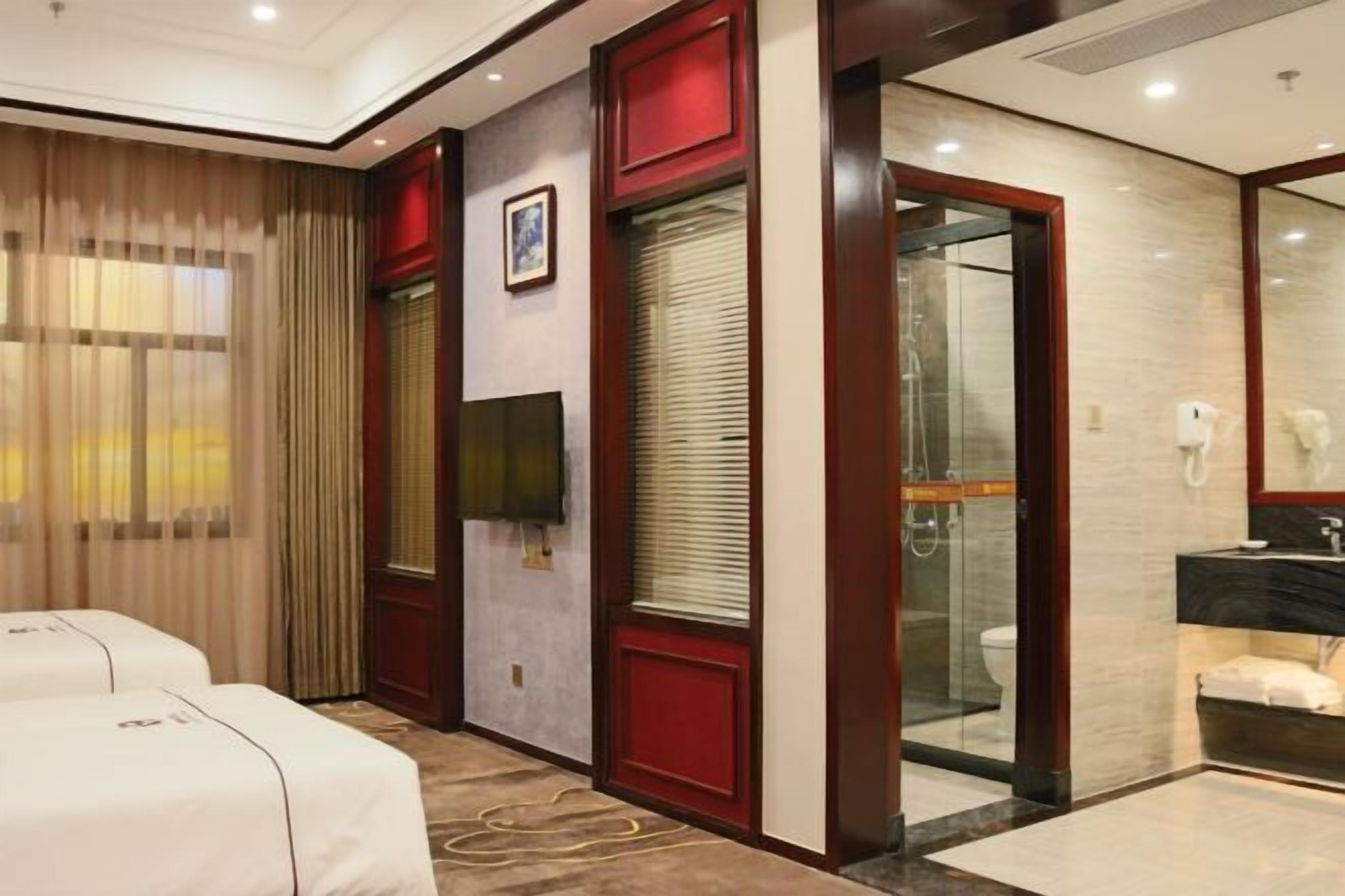 A hotel room with two beds, a bathroom with a glass shower, and a large mirror.