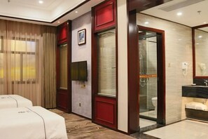 A hotel room with two beds, a bathroom with a glass shower, and a large mirror.