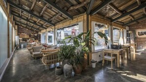 Um espaço amplo com vigas de madeira, área de cozinha, assentos e grandes janelas.