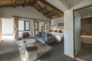 Una habitación de hotel moderna con una cama grande, un sofá, una mesita pequeña y un baño independiente.