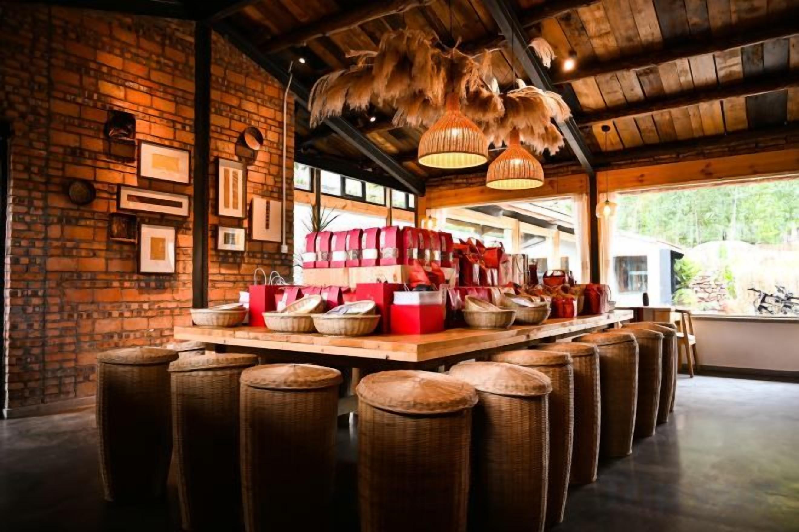 A rustic interior with a brick wall, wicker stools, and a wooden bar area with baskets and red containers.