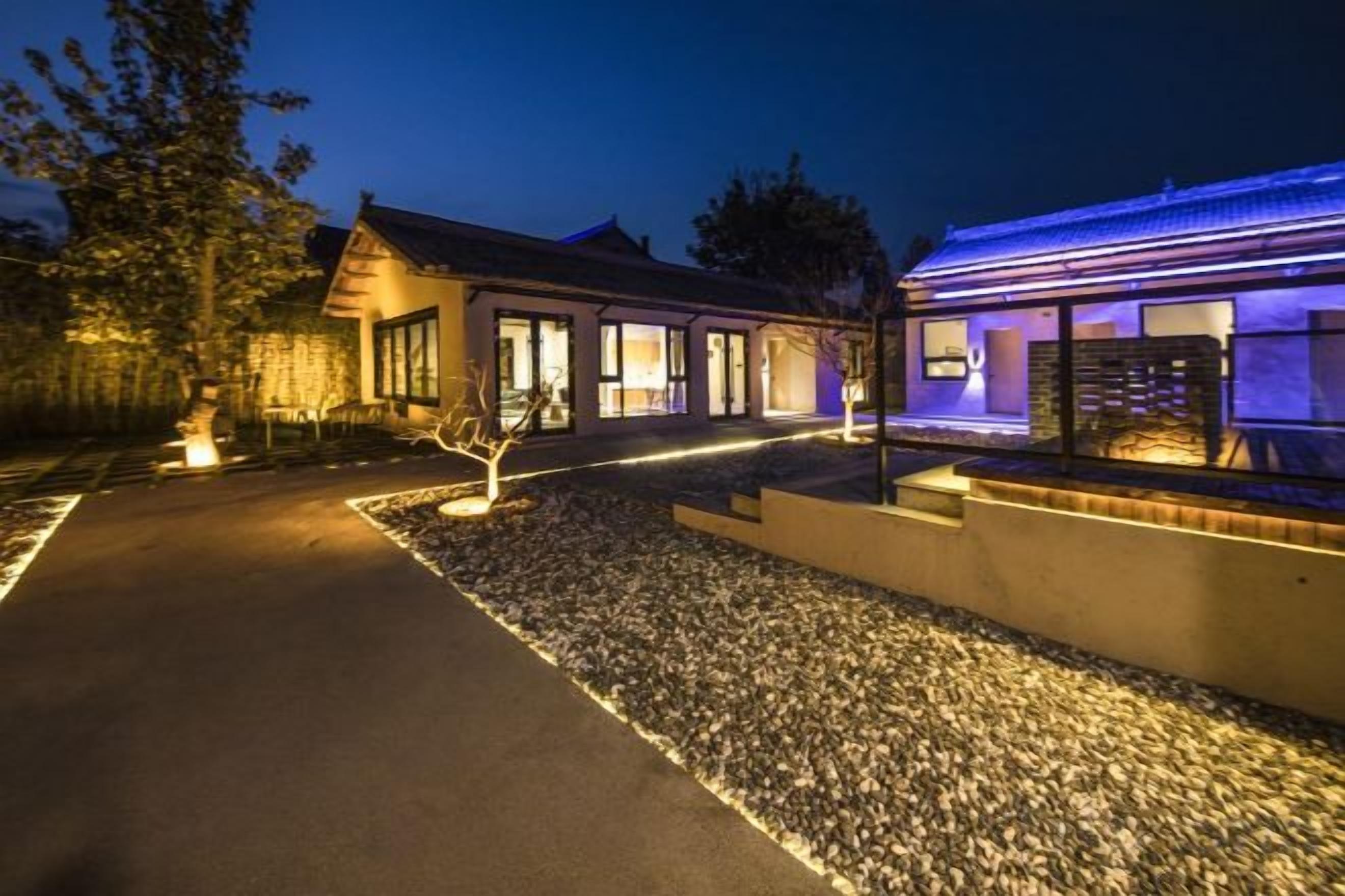 A modern house with a paved driveway, a gravel area, and a well-lit exterior.