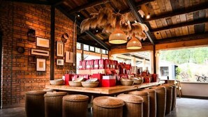 Um interior rústico com paredes de tijolos aparentes, um balcão de madeira comprido com banquetas e luminárias pendentes.