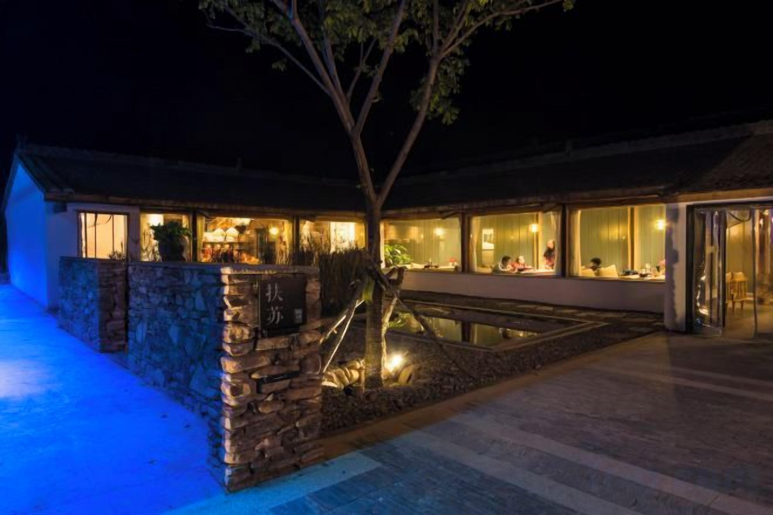 A building with a stone facade, a pond, and a well-lit interior.