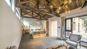 Um quarto espaçoso com teto alto, acabamento em madeira, uma janela grande e vista para um pátio externo.