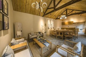 A spacious living area with a high ceiling, wooden beams, a central coffee table, sofas, and a dining area with chairs. - Poetic Cottages (Anze)