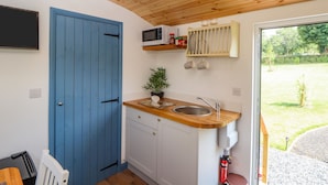 Cocina compacta con puerta azul, microondas, fregadero y ventana pequeña con vistas a un jardín.