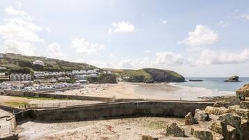 A coastal town with a sandy beach, a rocky outcrop, and residential buildings.