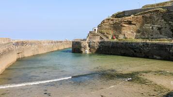 Une zone côtière avec un mur de pierre, un petit bâtiment et une vue dégagée sur la mer.