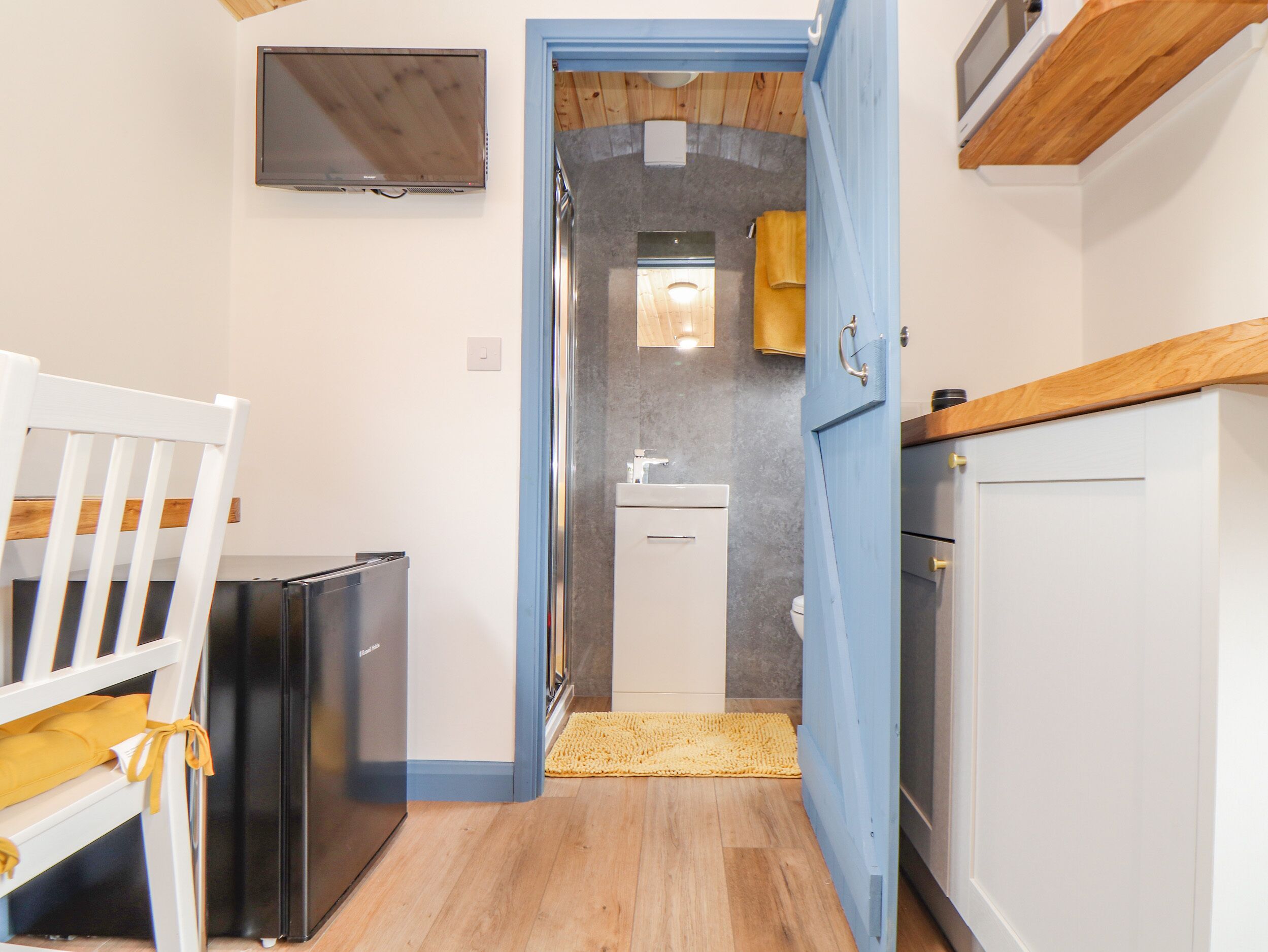 A compact kitchen with a refrigerator, a sink, and a wooden ceiling.