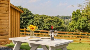 Una cabaña de madera con una mesa de picnic preparada para dos, que incluye una botella de vino y dos copas.