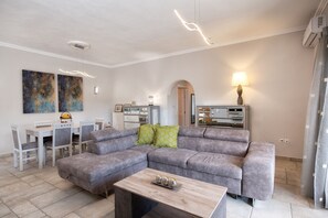 A modern living room with a grey sectional sofa, a wooden coffee table, and a dining area with a white table and chairs.