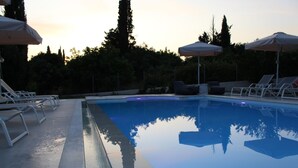 Piscina con sillas de descanso y sombrillas, rodeada de árboles.