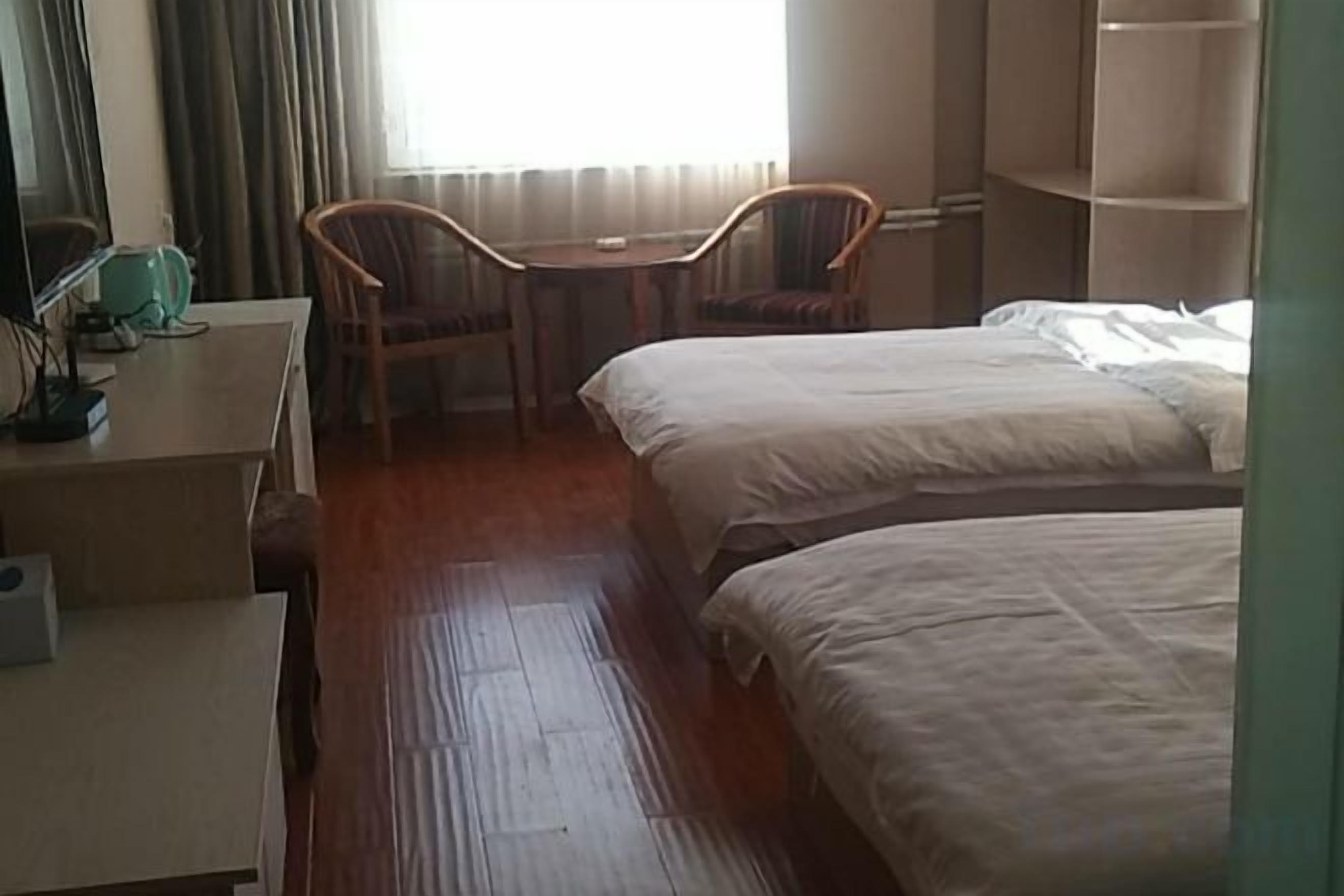 Una habitación de hotel con dos camas, un escritorio con silla y una ventana con cortinas.